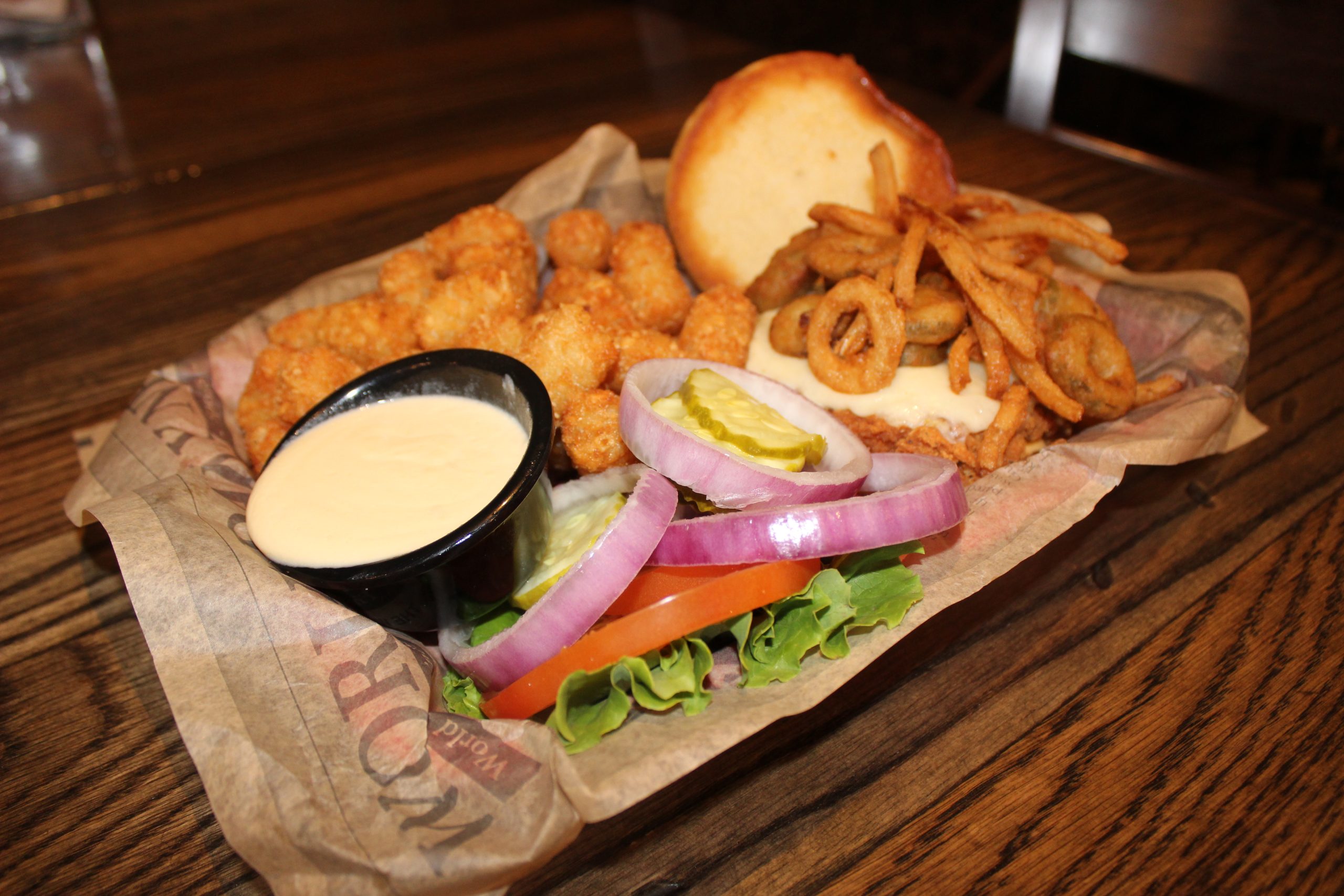 Spicy fried chicken breast topped with pepper jack cheese and fried jalapeño with onion tanglers. Served with sriracha mayo, lettuce, tomato, pickle, and onion on a brioche bun, with tater tots and a side of queso. 